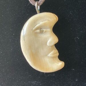 Carved bone or tusk half-moon face with crystal eyes. 2 sided. 18” silk cord.